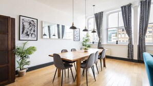 A dining area with a wooden table and chairs, a potted plant, and a large window with curtains. - Host Stay Exchange Street Living (Liverpool)