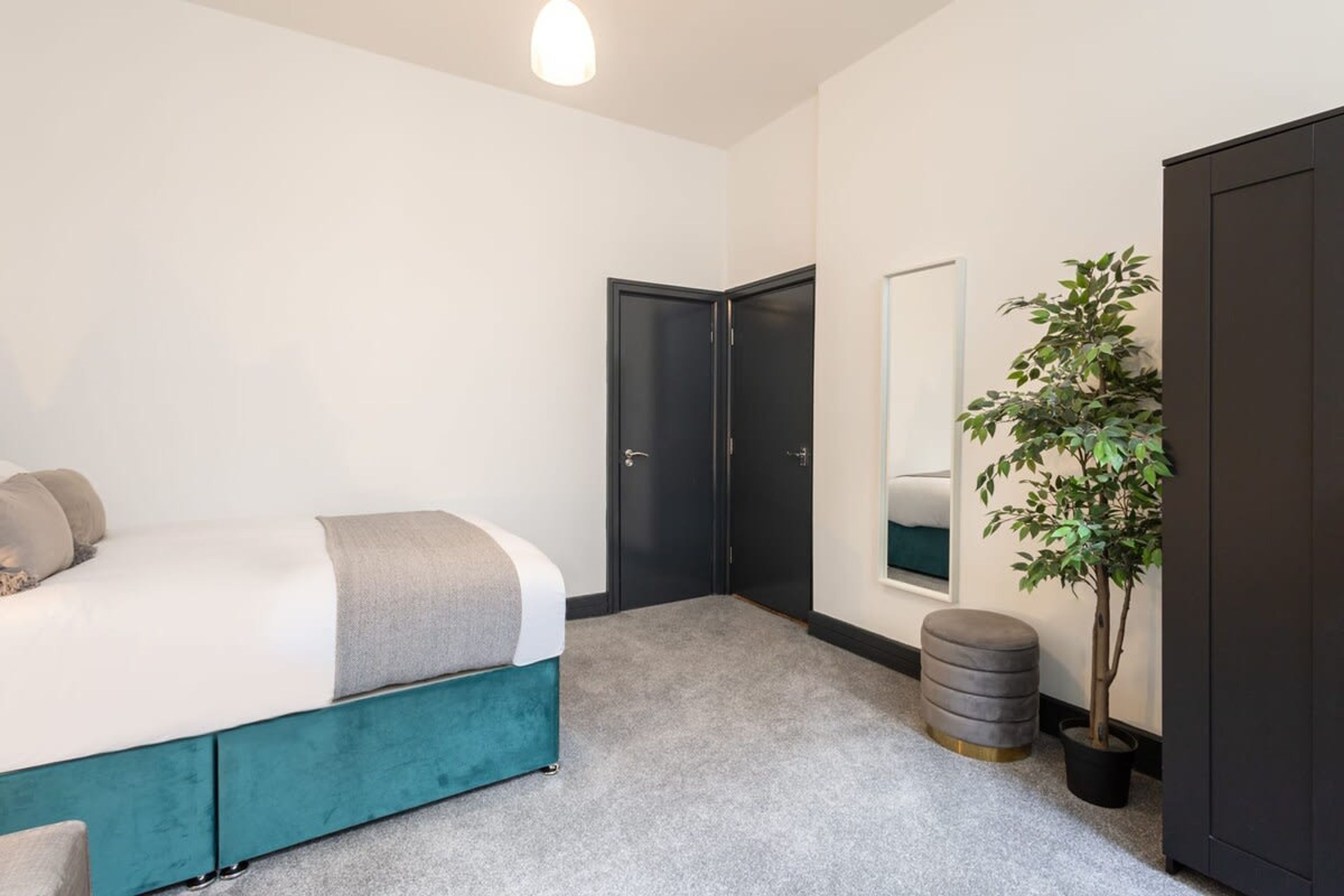 Un dormitorio con una cama, un armario oscuro, una planta en maceta y un espejo en la pared.