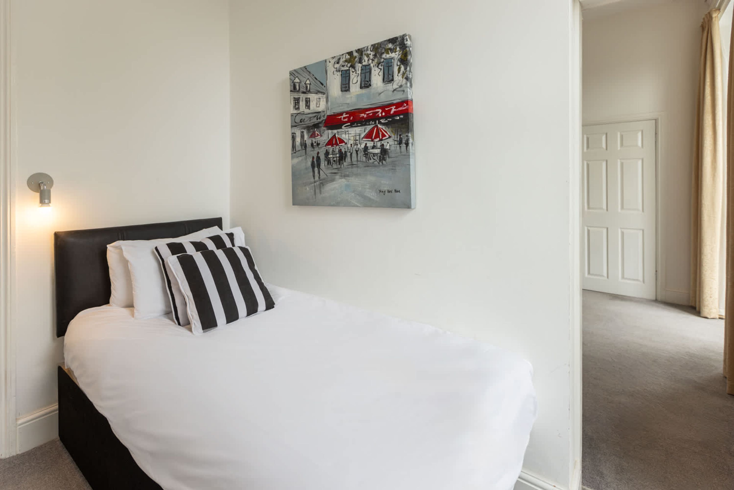 A bedroom with a bed, a wall-mounted artwork, and a door in the background.
