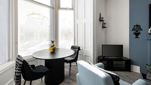 Un coin repas avec une table ronde, deux chaises, un téléviseur et un mur d’accent bleu.