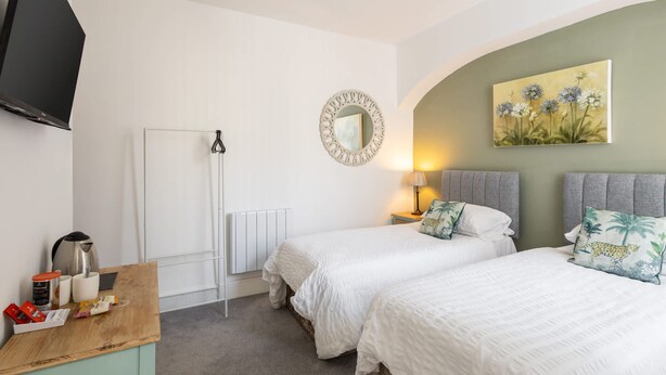 A hotel room with two beds, a wooden desk, a radiator, a television, and a painting on the wall. - Host Stay Goathland at the Sandbeck (Whitby)