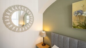 A room with a round mirror, a bedside lamp, a gray headboard, and a floral painting on the wall. - Host Stay Goathland at the Sandbeck (Whitby)
