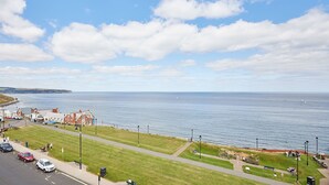A coastal town with a promenade, a sea view, and a small building with a red roof.