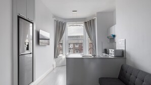 A modern kitchen with a built-in island, a grey sofa, and a view of the city through a window. - Host Stay Aberdeen Walk Apartment (Scarborough)