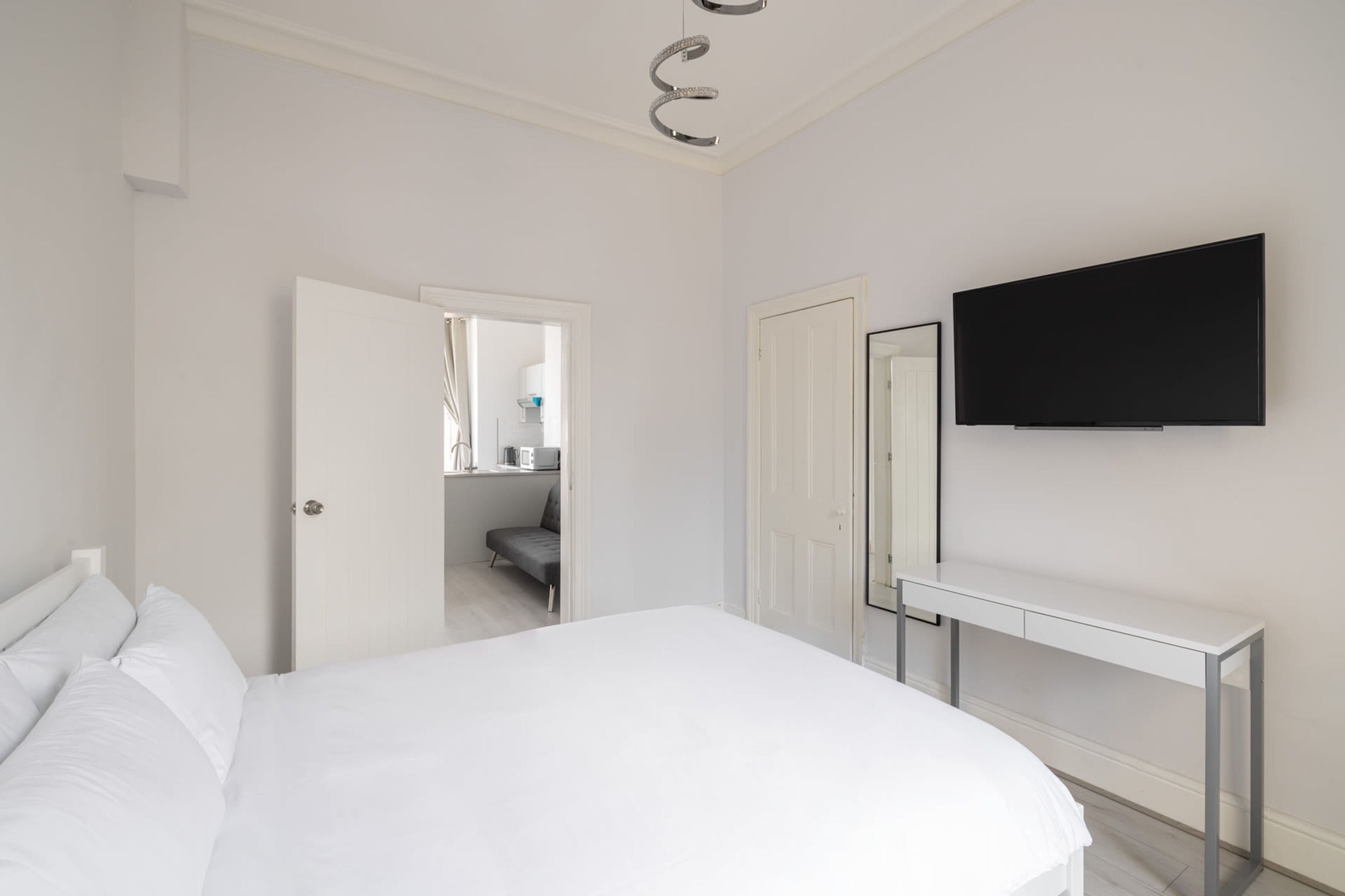 A bedroom with a bed, a TV mounted on the wall, a desk, and a door leading to a bathroom.