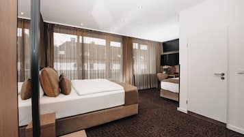 A modern hotel room with a large bed, a sofa, a desk, and a TV.