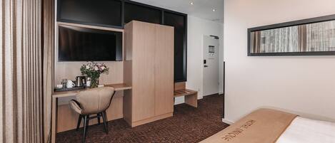 Una habitación de hotel con cama, escritorio, silla, armario, televisor y ventana.