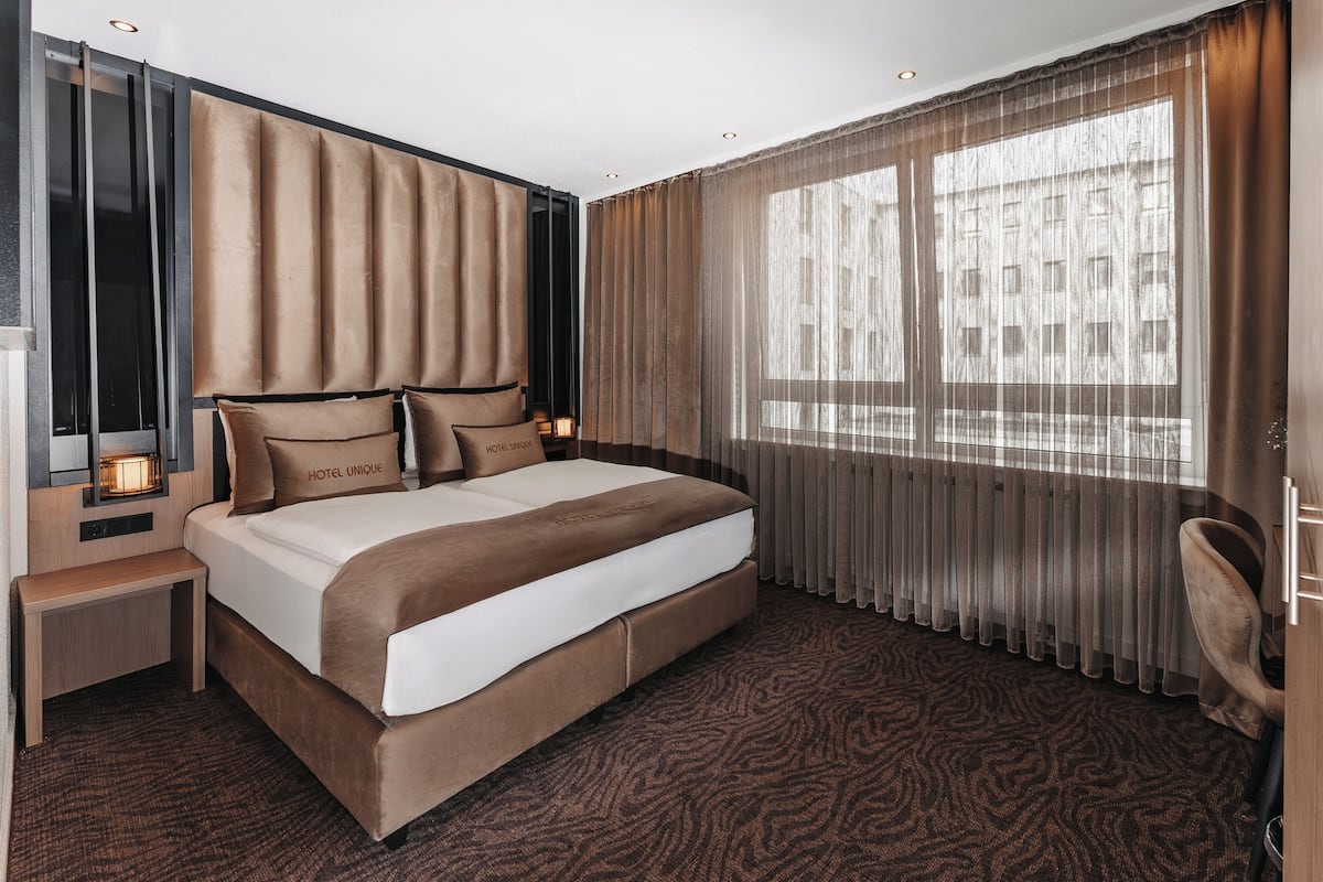 Une chambre d’hôtel moderne avec un grand lit, une table de chevet, une chaise et une fenêtre avec des rideaux.