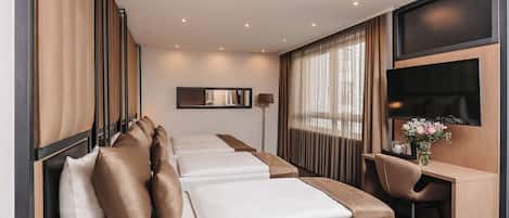 Habitación de hotel con una cama grande, un escritorio, una silla, un televisor y un ventanal con cortinas.