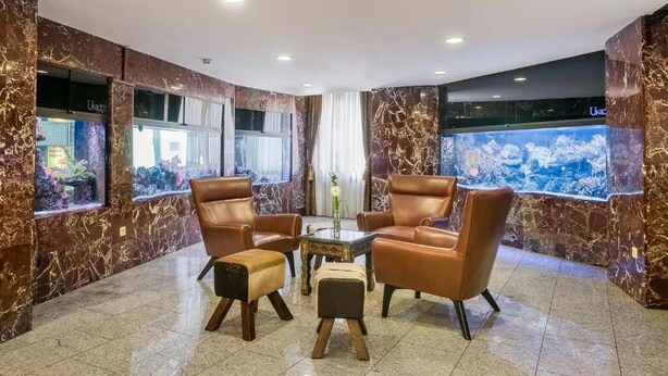 A lobby with marble walls, leather armchairs, a small table, and a fish tank. - Hotel Unique Majestic Hauptbahnhof (Dortmund)