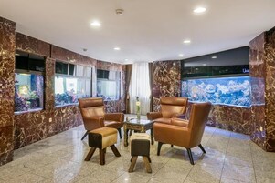 Un vestíbulo con paredes de mármol, sillones de cuero, una mesita y un acuario.