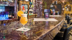 A bar with a marble countertop, a glass of beer with an orange slice and a straw, and a shelf with bottles in the background. - Hotel Unique Majestic Hauptbahnhof (Dortmund)