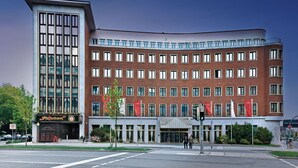 A modern building with a mix of brick and glass facade, featuring a prominent vertical glass section on the left. - Hotel Unique Majestic Hauptbahnhof (Dortmund)