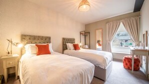 A bedroom with two beds, a nightstand, a lamp, a window with curtains, and a view of the outside.