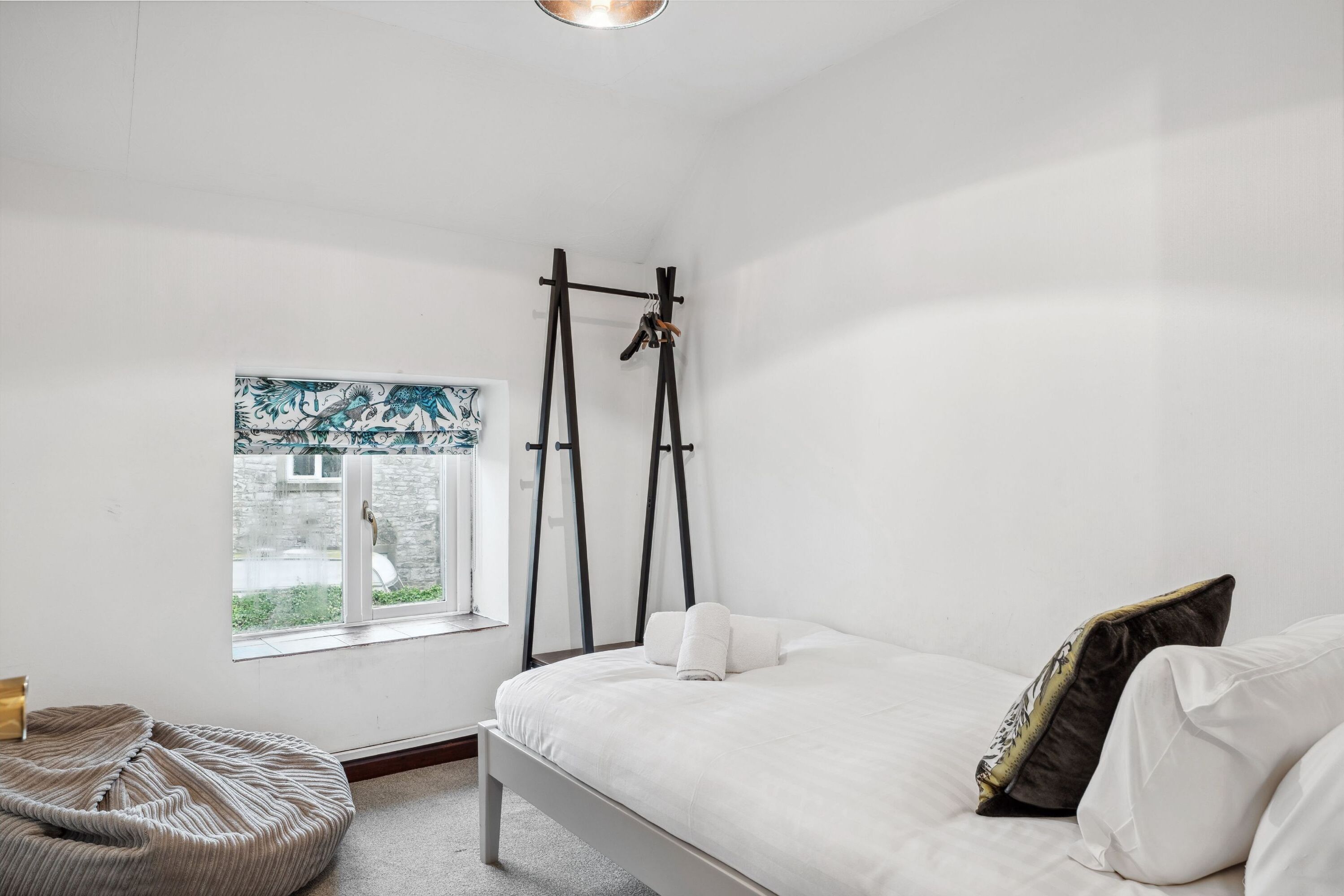 A bedroom with a bed, a window, a hanging shoe rack, and a bean bag chair.