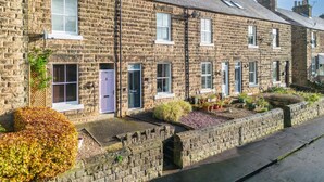A row of stone terraced houses with multiple windows, a small garden area, and a paved pathway.