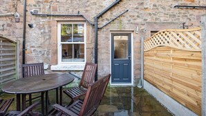 A stone building with a wooden table and chairs, a door, and a wooden fence.