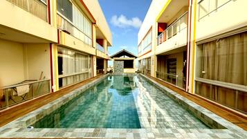 A swimming pool with a tiled deck, flanked by buildings with large windows and balconies.