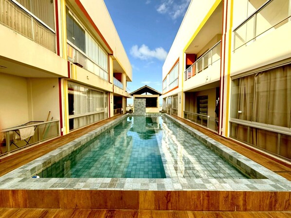 A swimming pool with a tiled deck, flanked by buildings with large windows and balconies. - SaltBeach Atalaia Residence Inn - M105 (Salinópolis)