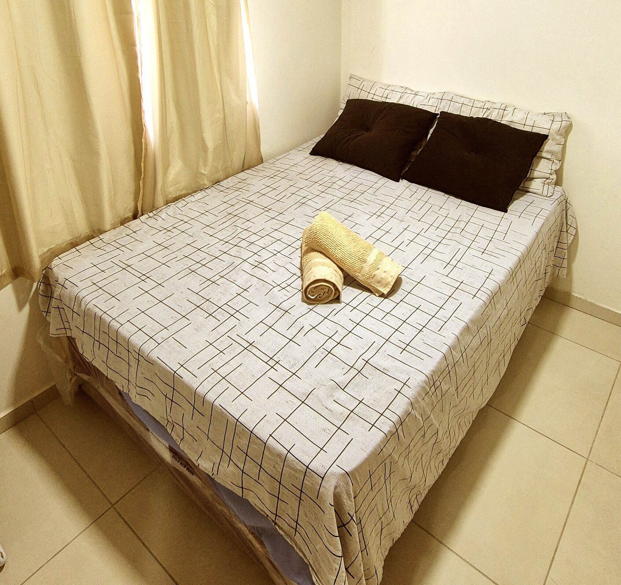 A single bed with a patterned bedspread, two pillows, and a rolled-up towel.