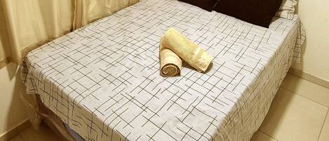 A single bed with a patterned bedspread, two pillows, and a rolled-up towel.