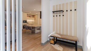 A modern interior with a wooden floor, a bench with a cushion, a dining area with a table and chairs, and a kitchen with appliances.