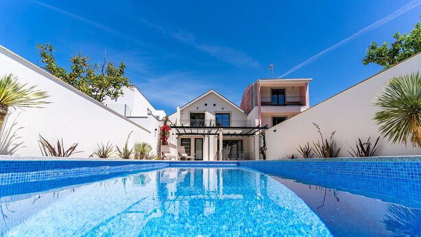 A swimming pool with a clear blue water surface, surrounded by white walls and potted plants.