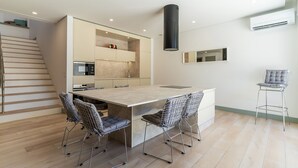 A modern kitchen with a central island, two bar stools, and a staircase.