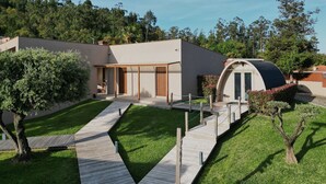 Ein modernes Haus mit einer Holzterrasse, einem kleinen Baum und einer geschwungenen Struktur.