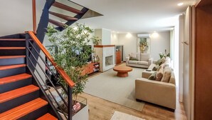 Ein modernes Wohnzimmer mit Treppe, einer Sofagarnitur, einem Couchtisch und einer großen Topfpflanze.