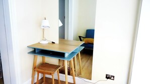 A small wooden desk with a lamp, a chair, and a mirror reflecting a blue sofa and a wall socket. - Xxxxxxxxxxxxxxxxxxxxxxxxxxxxxxxxxxxx (London)