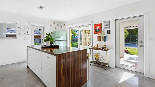 A modern kitchen with a central island, white cabinetry, and a view to the outdoors. - Palm Springer - Heated Salt Water Pool Steps from the Drive (Wilton Manors)