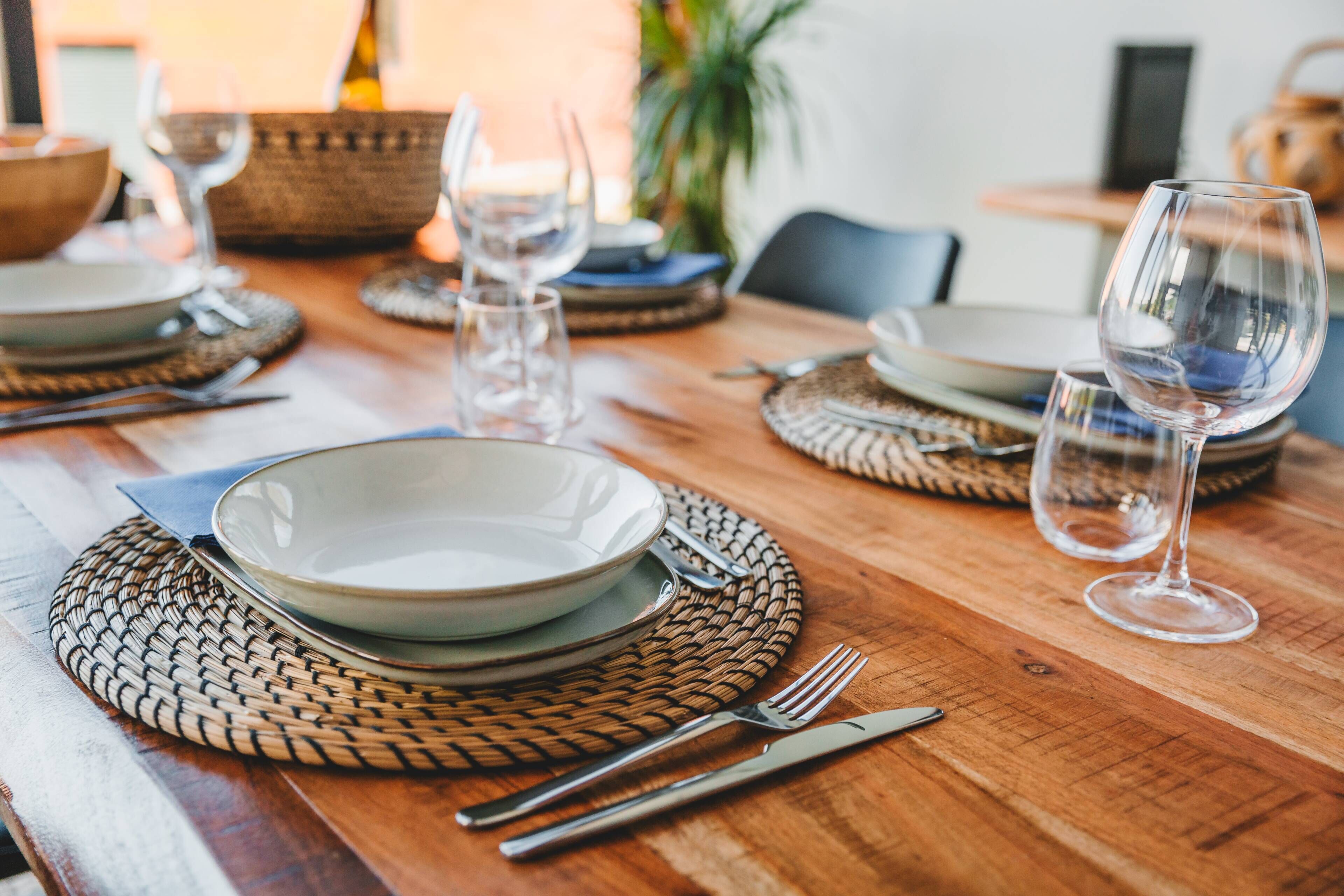 Una mesa de comedor de madera dispuesta con platos, cubiertos y copas de vino.