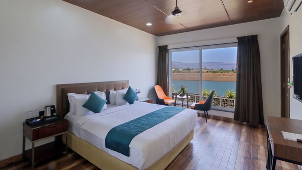A hotel room with a large bed, a desk, a chair, and a view of a body of water.