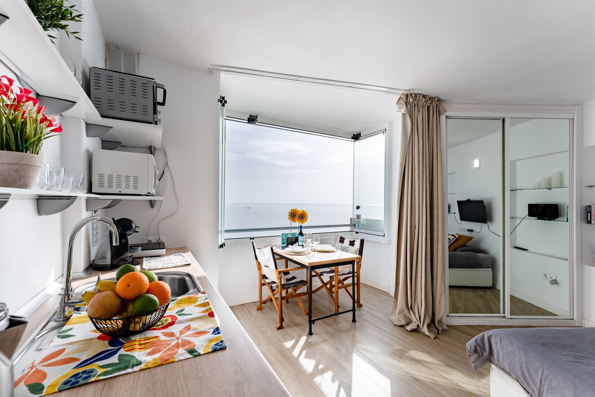 Een compacte woonruimte met een kitchenette, een eethoek met uitzicht en een glazen schuifdeur naar een balkon.