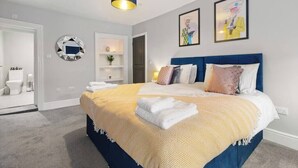 Un dormitorio moderno con una cama grande, un cabecero azul y un espejo circular en la pared.