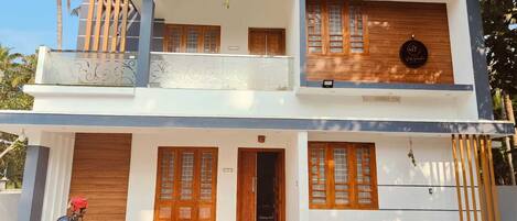 A two-story modern house with a balcony, wooden doors, and potted plants.