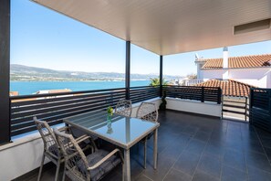 A balcony with a glass table and wicker chairs, overlooking a coastal view with a clear sky. - Stylish studio Arya 2 - w/ sea view, 150m to beach (Mastrinka)