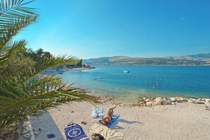 Ein Strand mit klarem Wasser, sandigem Ufer und einer Person, die sich sonnt.