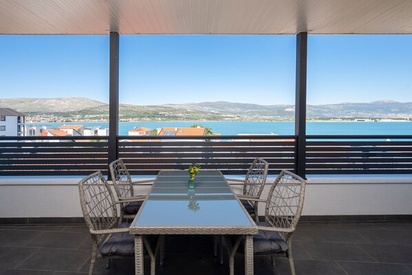 A terrace with a glass table and wicker chairs, overlooking a coastal town and sea. - Stylish studio Arya 2 - w/ sea view, 150m to beach (Mastrinka)