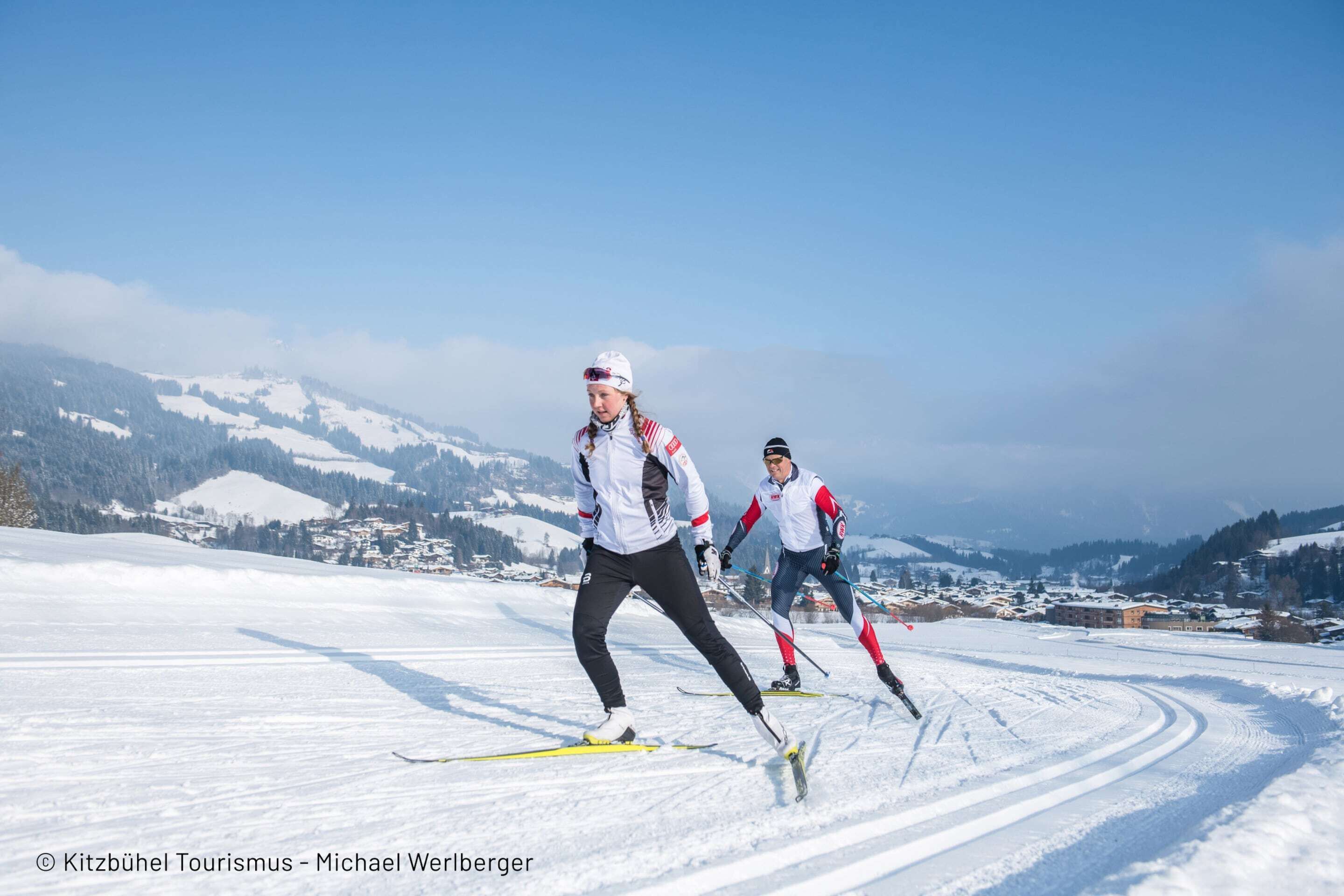 Zwei Skifahrer auf einer verschneiten Piste vor einer Bergkulisse.