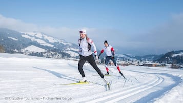 Twee skiërs op een besneeuwde piste, met een bergachtig landschap op de achtergrond.