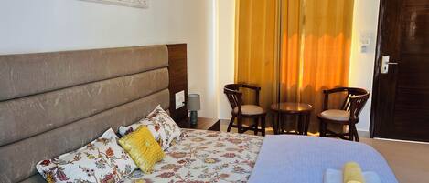 A hotel room with a bed, a nightstand, a lamp, two chairs, a door, and a window with curtains.
