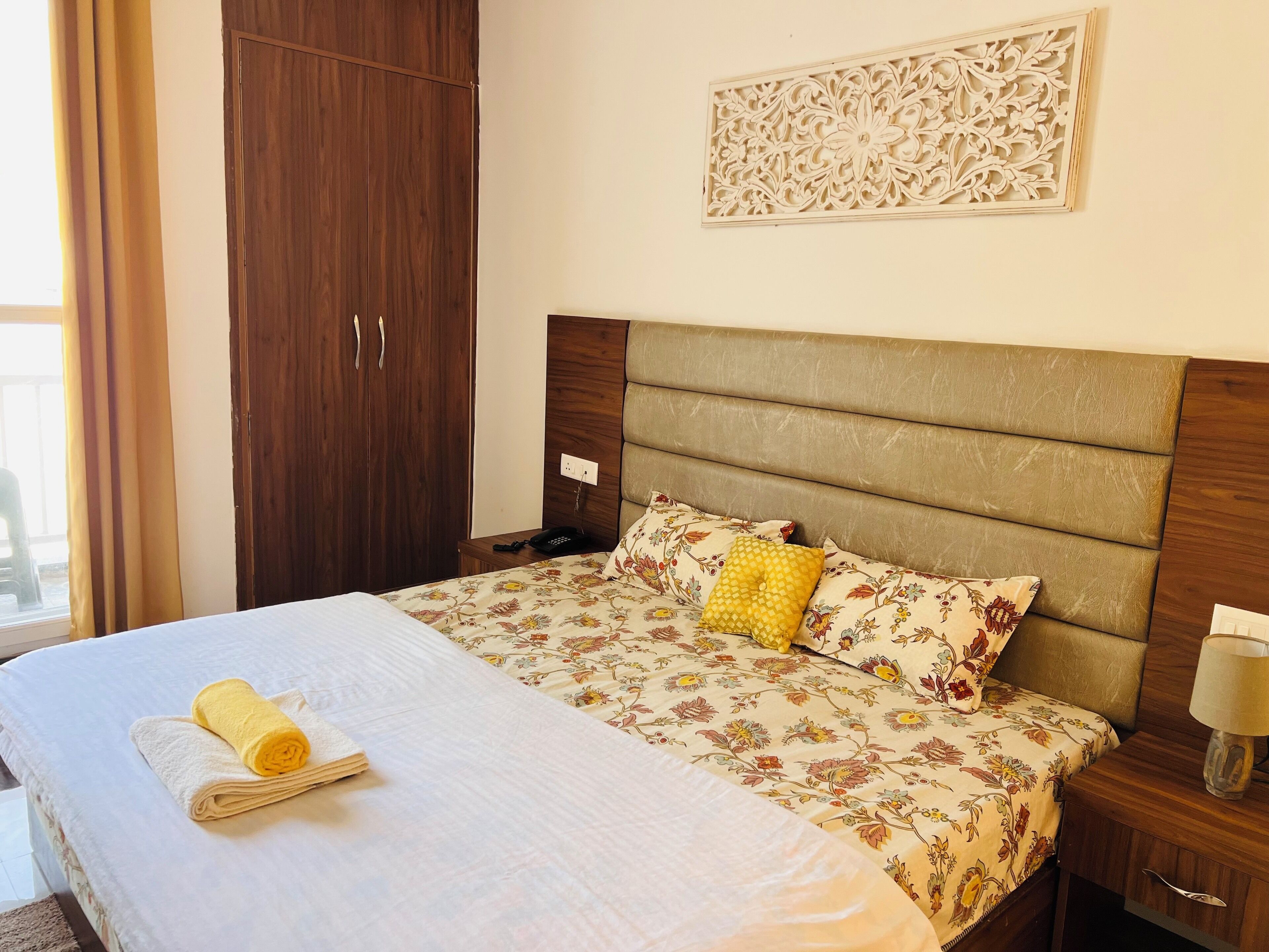A neatly made bed with a floral bedspread and a rolled towel.