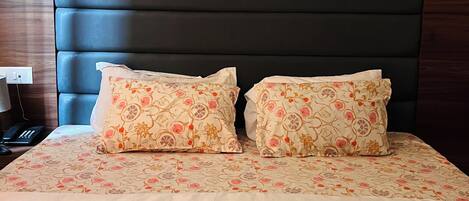 A neatly made bed with floral-patterned pillows and a folded towel.