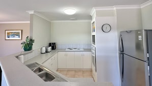 Moderni keittiö, jossa on valkoiset kaapit, ruostumattomasta teräksestä valmistettu jääkaappi, sisäänrakennettu uuni ja mikroaaltouuni.