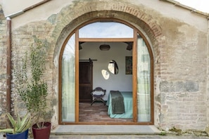 Un portail en arc donnant sur une piĂšce oĂč se trouvent un lit, une chaise et un miroir.