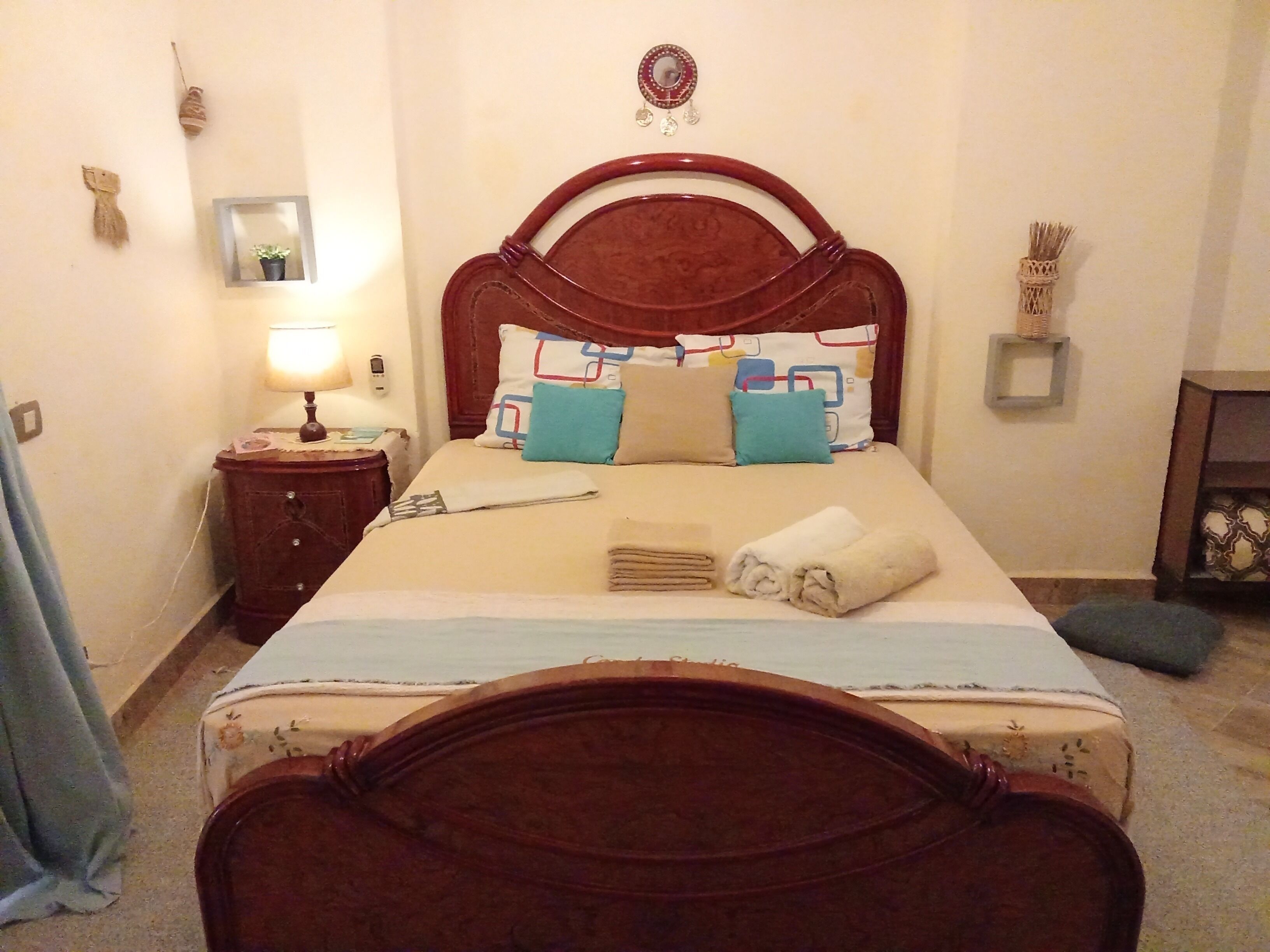 A neatly made bed with a wooden headboard, a bedside table with a lamp, and a small mirror on the wall.