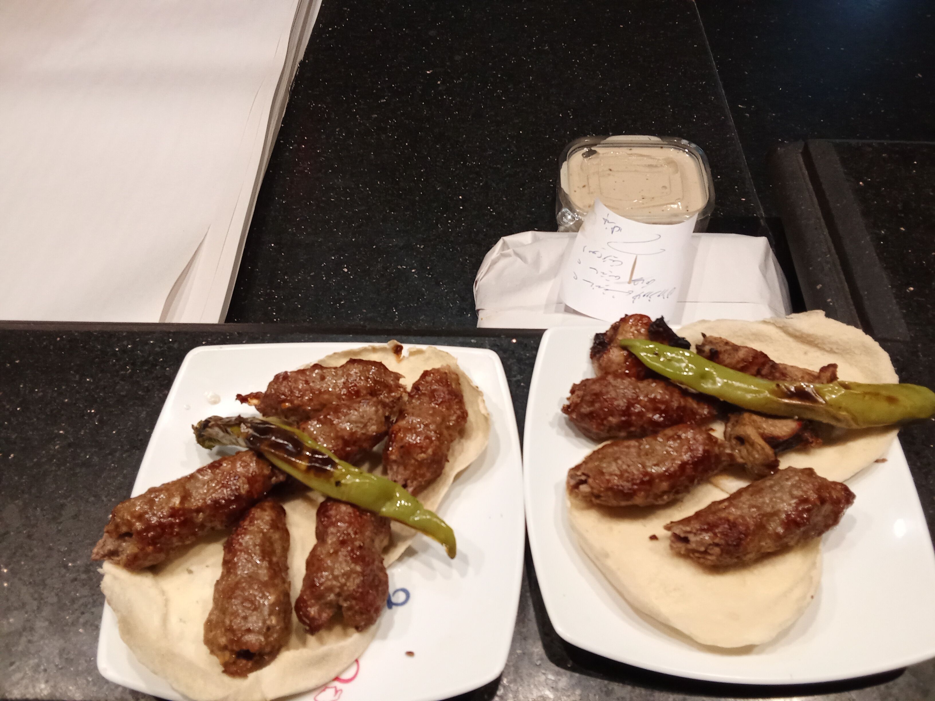 Dos platos de brochetas de carne con pan plano y una salsa al lado.