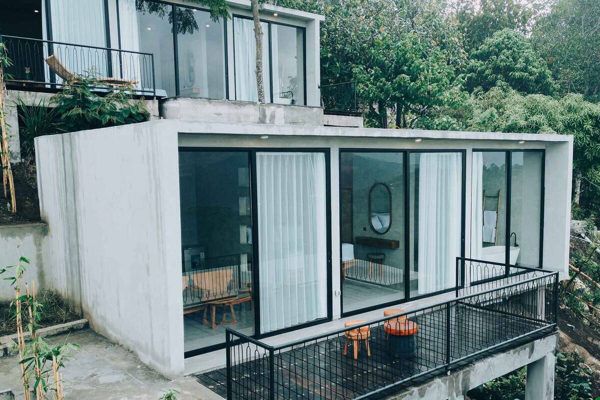 Une maison moderne à plusieurs niveaux, dotée de grandes fenêtres en verre et d’un balcon.
